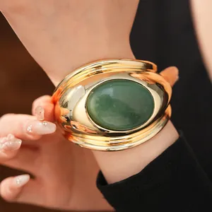 Exaggerated gold-tone twisted open cuff bangle featuring a large oval green stone inlay