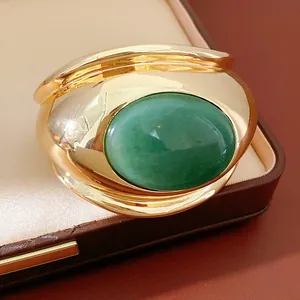 Close-up of a chunky gold twisted cuff bracelet featuring a large oval green stone.