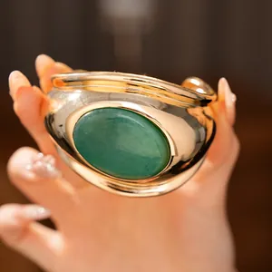 Detailed view of a wide twisted gold cuff bracelet featuring a large green oval stone inlay