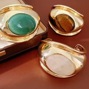 Macro view of chunky gold cuff bracelets featuring large oval tiger's eye and rose quartz stones