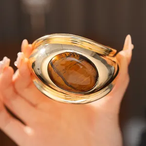 Macro view of a chunky gold cuff bracelet featuring a large oval tiger's eye stone.