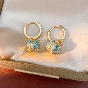 Detailaufnahme von 14k vergoldeten Creolen mit türkis besetzten Kürbisanhängern.