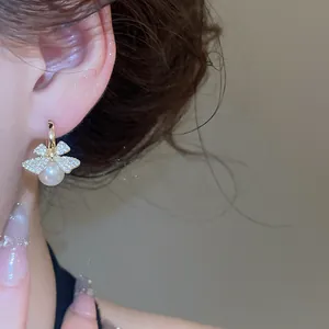 Close-up detail of an elegant zircon bow earring with white pearl drop on a model