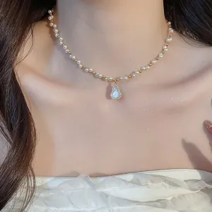 Macro detail of a vintage pearl necklace featuring an iridescent zircon gourd pendant on a model