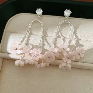 Primo piano di orecchini a nappa con fiori in resina rosa e zirconi su vassoio beige