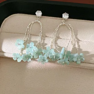 Dettaglio di orecchini a nappa in argento con ciondoli a fiore in resina verde e zirconi