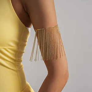 Close-up van een gouden metalen armring met elegante lange kettingkwastjes aan arm.