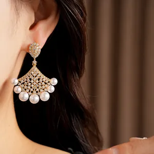 Macro detail of luxury 18K gold plated fan earrings featuring pavé zircons and white pearls
