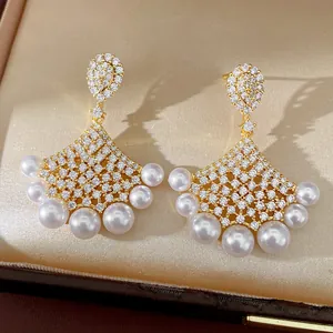 Detailed macro view of fan-shaped gold-plated earrings with pavé zircons and pearls