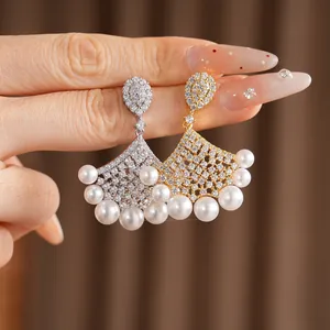 Close-up of elegant fan-shaped earrings with cubic zirconia and pearls in gold and silver.
