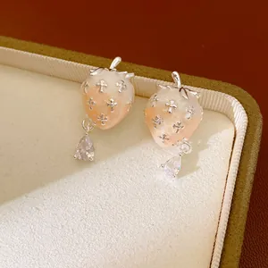 Close-up of strawberry earrings with silver crosses and teardrop zircon pendants.