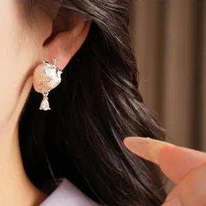 Detail showing a delicate strawberry stud earring with a dangling zircon teardrop.