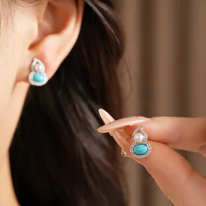 Detailed view of silver gourd stud earrings with cubic zirconia, pearl and turquoise