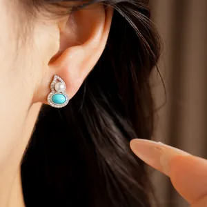 Elegant macro view of a silver hulu stud earring with pearl and turquoise on an ear.