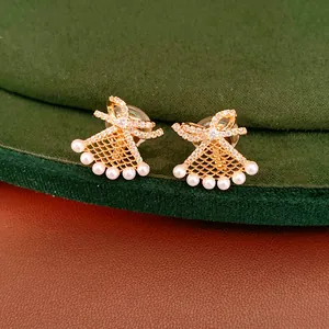 Macro view of gold-plated bowknot fan-shaped earrings adorned with delicate white pearls