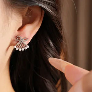 Macro detail shot of elegant gold plated bow and fan-shaped pearl drop earrings on ear