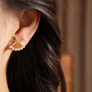 Close-up detail of an elegant gold bow fan-shaped earring with pearls worn on an ear