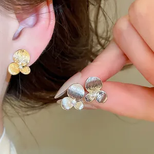 Détail des boucles d'oreilles fleur texturées avec zircon sur l'oreille et sur la main