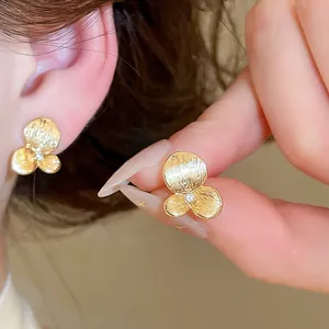 Gros plan de boucles d'oreilles fleurs dorées avec pétales texturés et zircon central