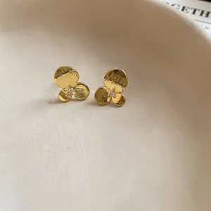 Vue macro de boucles d'oreilles fleurs en métal doré martelé avec zircon central.
