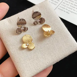 Détail de boucles d'oreilles fleurs aux pétales texturés or et argent avec zircon.