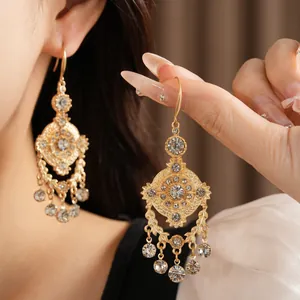 Détail de boucles d'oreilles lustres dorées de style palais ornées de strass brillants.