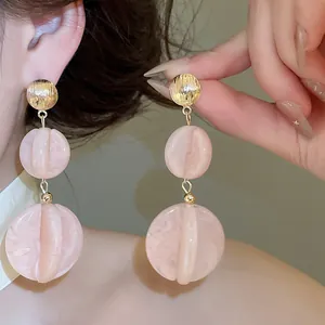 Primer plano de pendientes bohemios de acrílico rosa con textura de mármol y detalles dorados.
