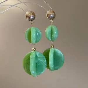 Detalle de pendientes colgantes de acrílico mármol verde con tuercas metálicas de oro.