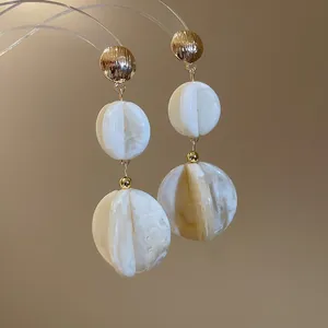 Primer plano de pendientes de acrílico jaspeado blanco con elegantes pernos dorados
