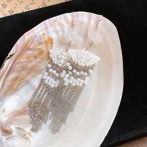 Close-up of elegant Chinese style flower fan earrings with long silver tassels on a shell.