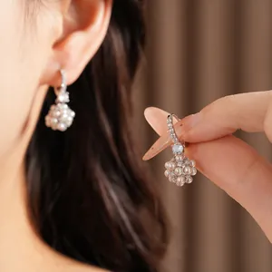 Close-up detail of elegant zircon pearl cluster earrings being held and worn on ear