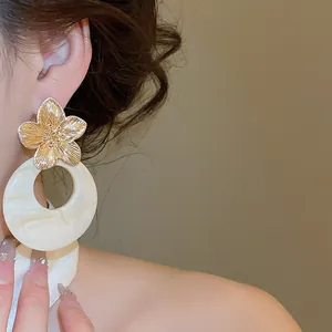 Close-up of gold flower and marbled resin hoop earrings on a model's ear