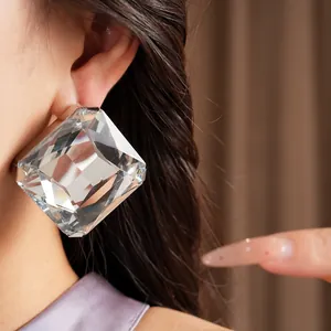 Gros plan de boucles d'oreilles clous carrées géantes en cristal clair sur une oreille femme