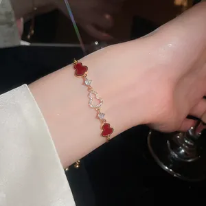 Close-up of a gold-plated bracelet with red gourd charms and zircons on a wrist.
