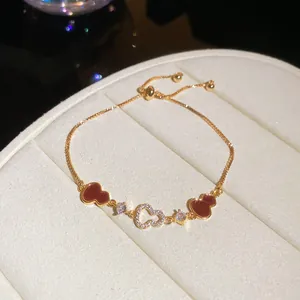 Detailed macro shot of an 18k gold plated bracelet with zircon heart and red gourd charms.