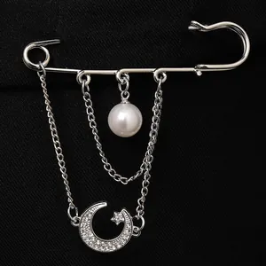Close-up of a silver safety pin brooch with pearl and crystal moon star charms.