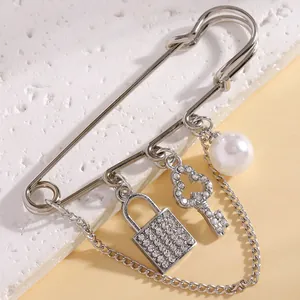 Close-up detail of rhinestone encrusted lock and key charms on a silver pearl safety pin brooch