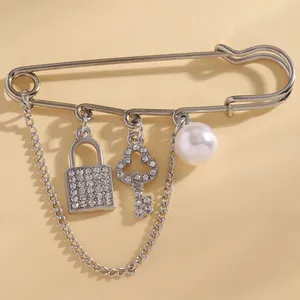 Macro view of a silver safety pin brooch with sparkling lock, key, and pearl charms.