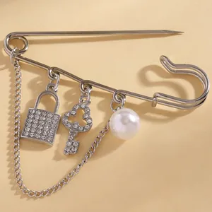Detailed macro view of a silver safety pin brooch with rhinestone lock, key and pearl charms