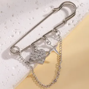 Close-up of a silver safety pin brooch with rhinestone heart and star charms on a chain.