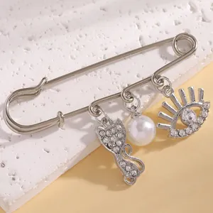 Detailed view of silver safety pin brooch with pearl, rhinestone cat and evil eye charms