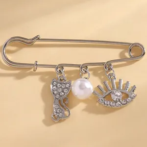 Detailed macro view of a silver safety pin brooch with cat, pearl, and evil eye crystal charms