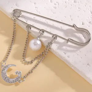 Detailed close-up of a silver safety pin brooch with star, moon, and pearl dangles