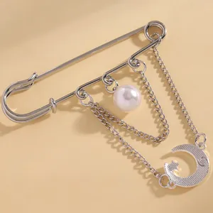 Detail view of a silver-tone safety pin brooch featuring a moon charm and pearl decoration