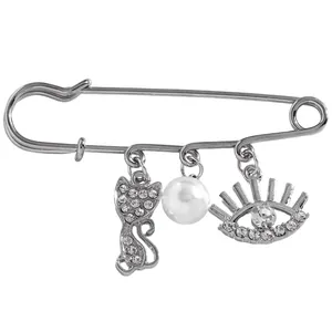 Close-up of silver safety pin brooch featuring dangling pearl, rhinestone cat and evil eye charms