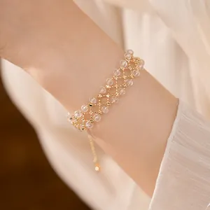 Vista dettagliata di un elegante bracciale in oro intrecciato con perle di vetro al polso