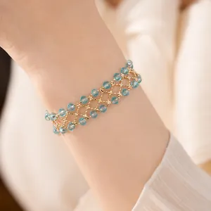 Primo piano di un bracciale a maglia dorata con perle di vetro azzurre su un polso