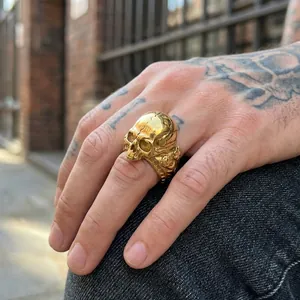 Detailed view of a gold-colored punk skull ring worn on a tattooed hand in natural light