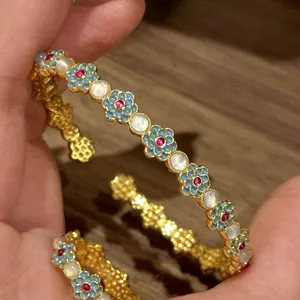 Detailed view of vintage gold bangle with blue enamel flowers and cat's eye stones
