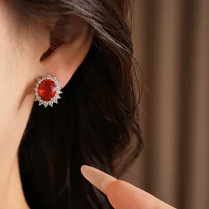 Vue détaillée de boucles d'oreilles ovales avec pierre rouge et halo de zircons étincelants.